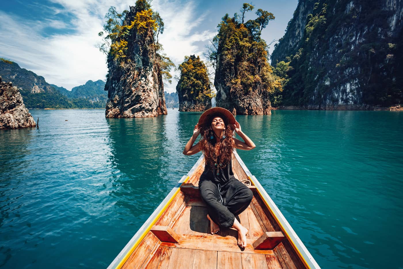 Woman in a sun hat relaxing at the bow of a longtail boat among limestone islands