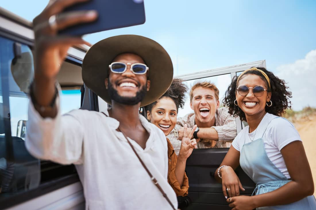 Group of friends laughing and taking a selfie beside a safari vehicle