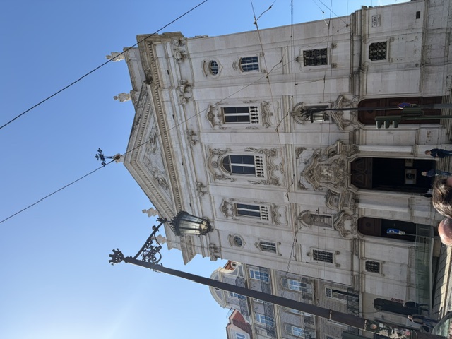 Ornate carved baroque church facade on a cobbled street in downtown Lisbon, with a vintage street lamp and tram cables overhead