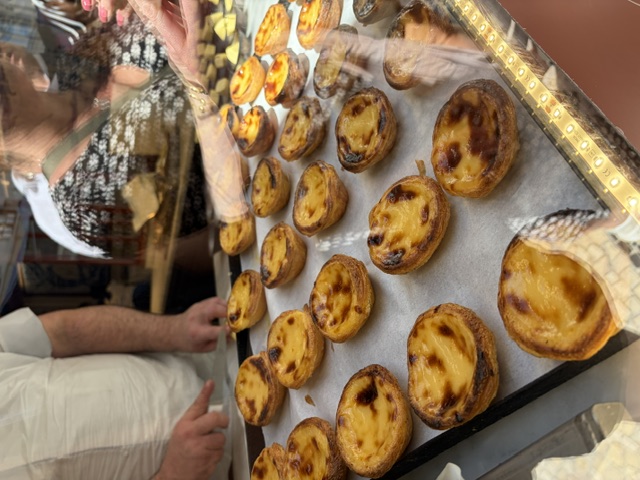 Trays of freshly baked golden pastéis de nata custard tarts on display in a Lisbon bakery window