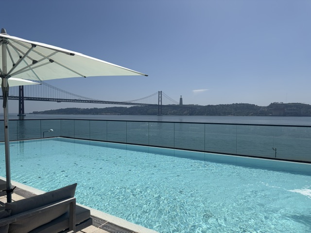 Infinity pool with white parasol and sun loungers overlooking the River Tagus and the iconic 25 de Abril Bridge in Lisbon